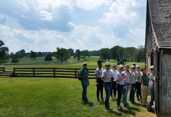 Gruppe von Jugendlichen und Erwachsenen vor einem Gebaeude in einer offenen Gruenflaeche