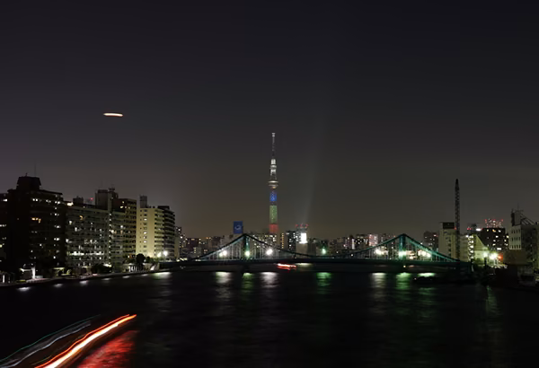 Naechtliche Stadtansicht am Wasser mit Bruecke, Lichtspuren und beleuchtetem Turm